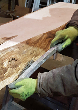 Photo of cleaning the edge of a live edge slab with a wire bristled brush